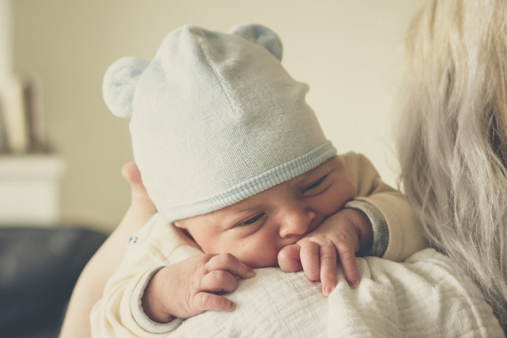 parent holding a newborn baby dressed in a hat