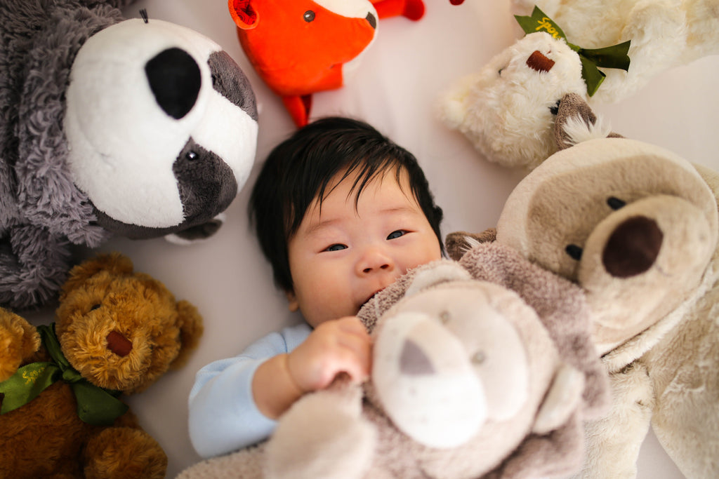baby lying down surrounded by soft toys 